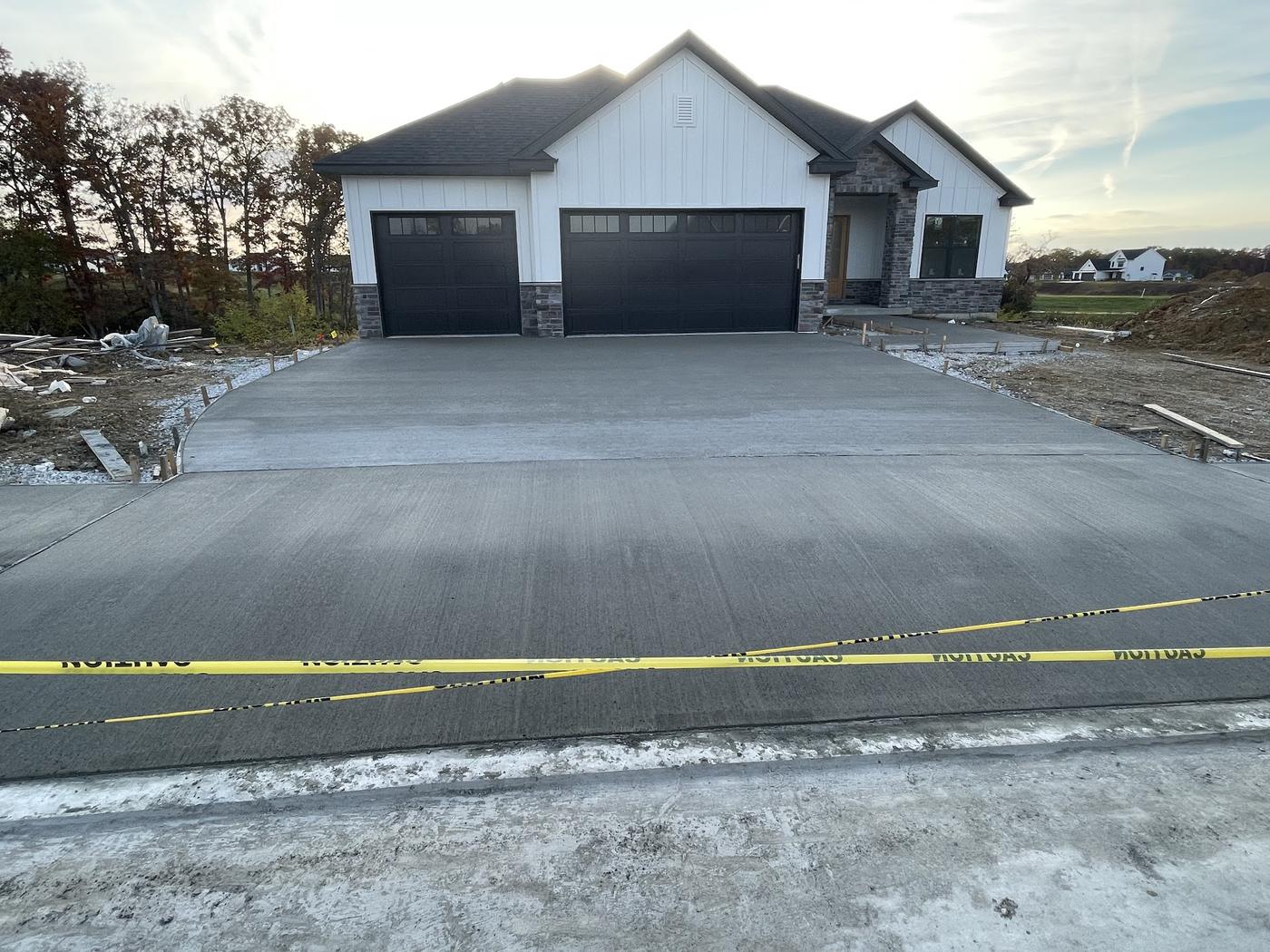 A finished concrete driveway and apron at a new house, broom finished and scored into panels, with caution tape still across it