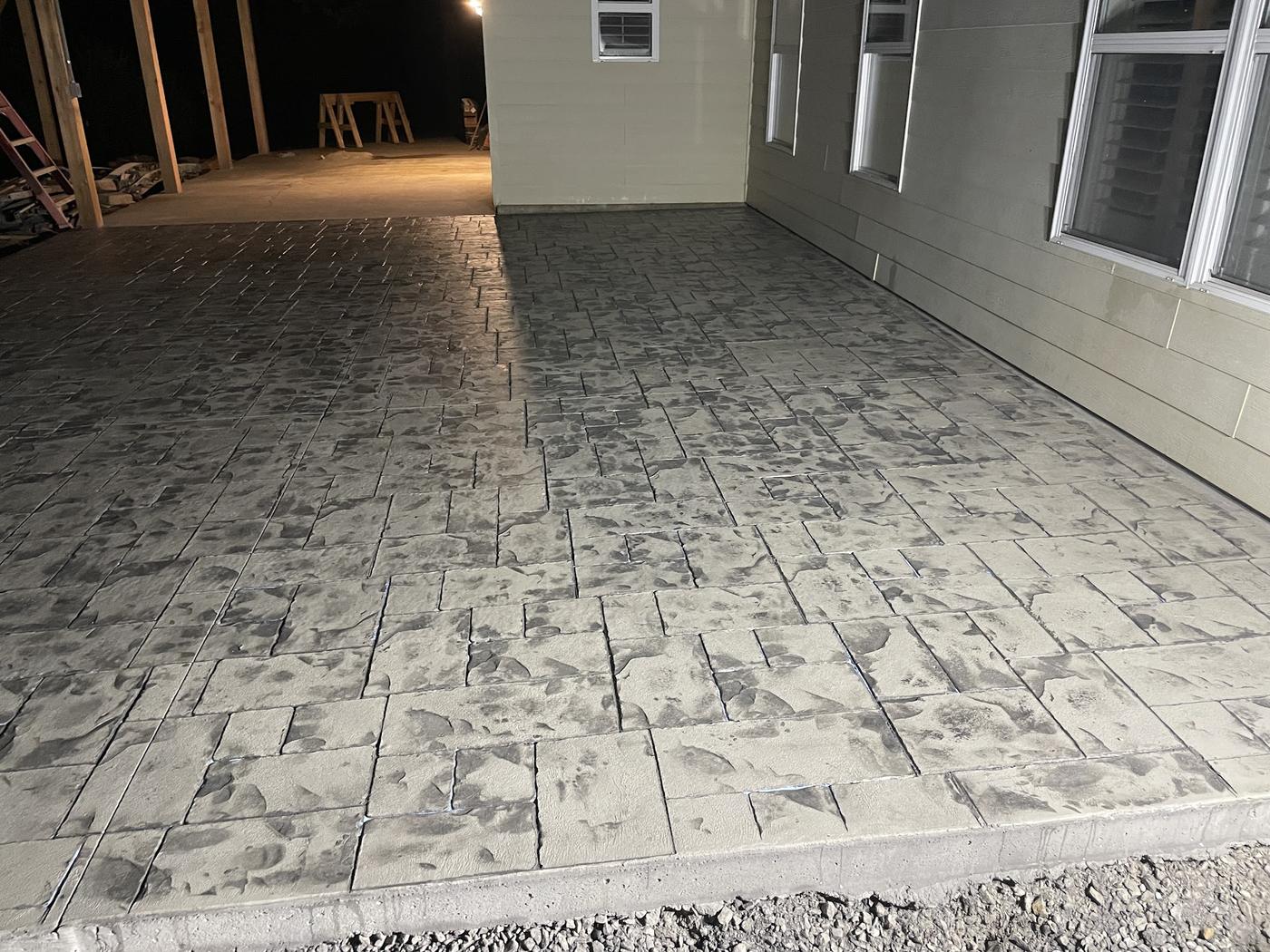 A patio stamped in a cut-stone pattern and worked with a darker release. It is concrete, all of it, which is the whole trick.